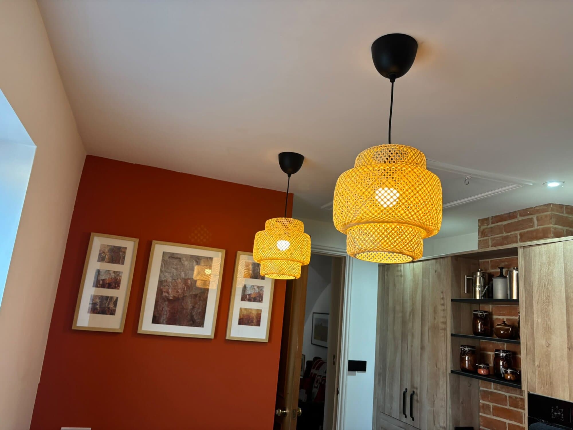 Two woven pendant lights hung over a kitchen with a brick feature wall